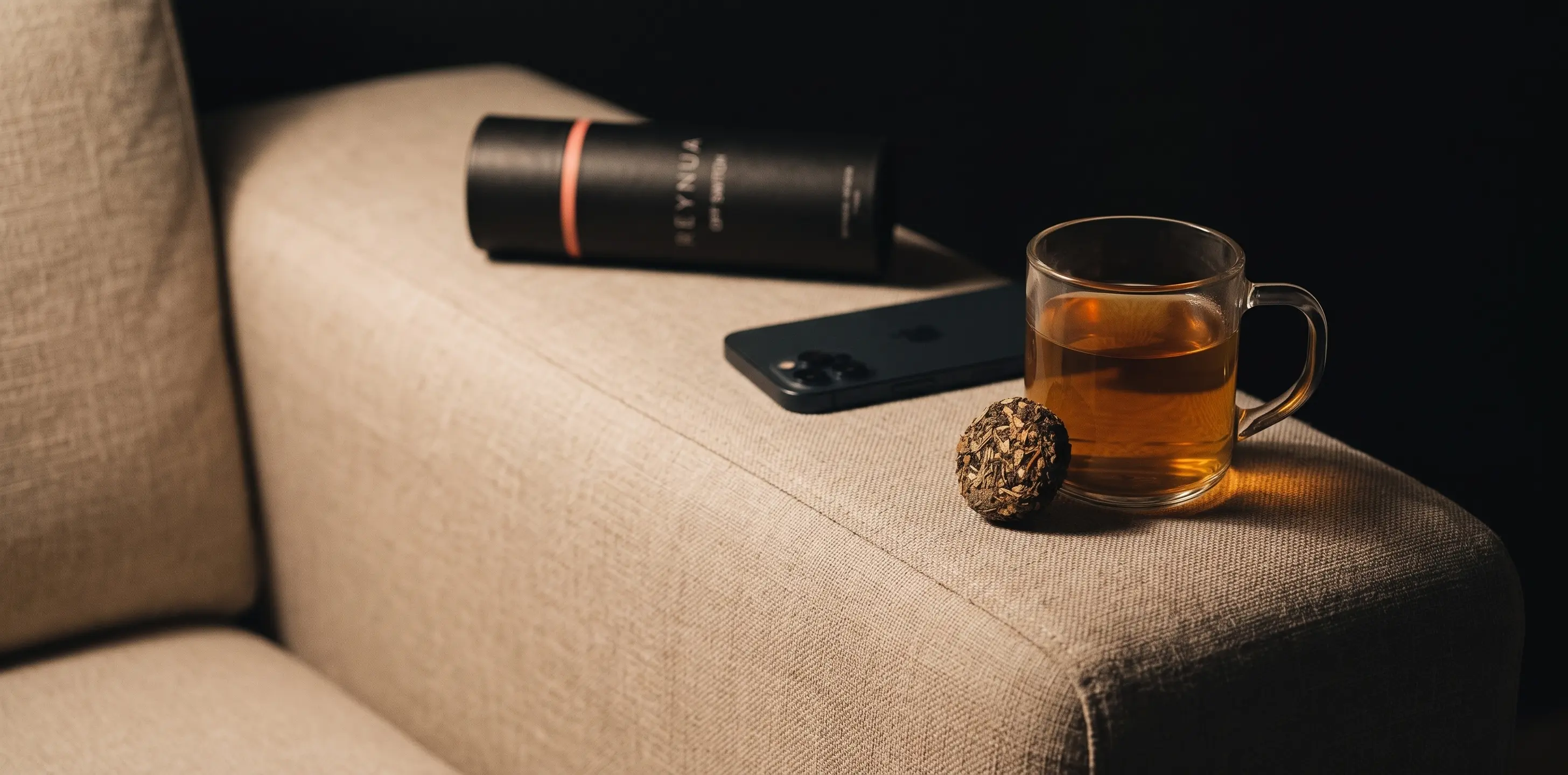 Eine Tasse auf der Sofalehne, daneben das Handy mit dem Bildschirm nach unten